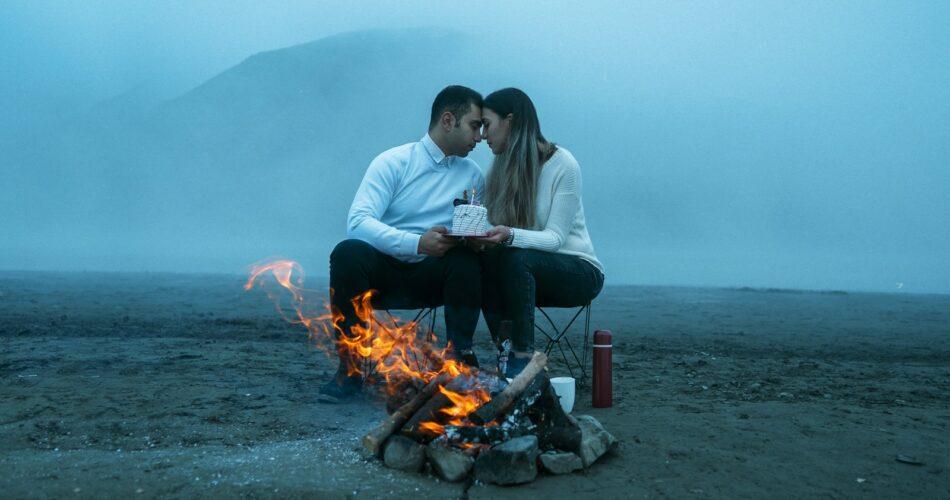 a man and woman sitting next to a campfire