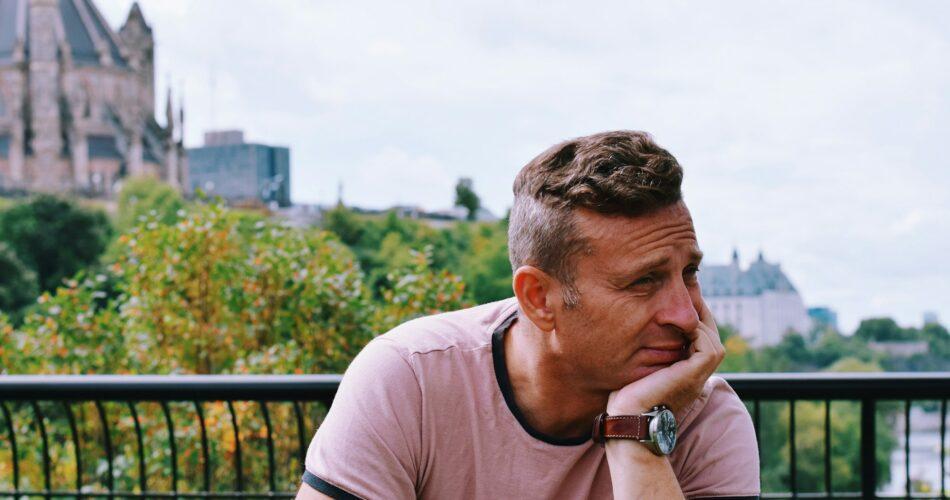 A man is sitting on a park bench deep in thought, contemplating