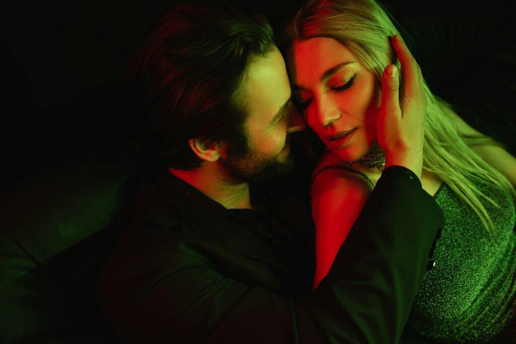 Smiling man touching seductive girlfriend with lighting isolated on black